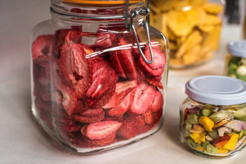 A glass jar of freeze dried strawberries near jars with other types of freeze dried fruits and vegetables