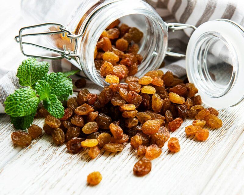 A glass jar of raisins, with most spilling out onto the table