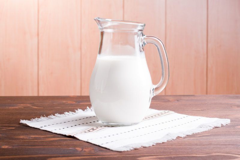 A glass jug of buttermilk on a wooden table with a cloth underneath it. 