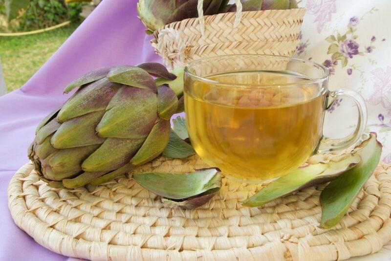 A glass mug of artichoke tea next to an artichoke flower