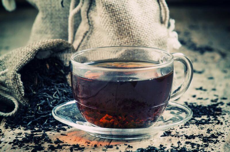 A glass mug of black tea, with black tea leaves scattered around