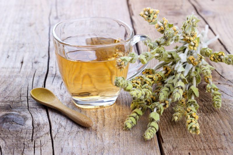 A glass mug with Greek mountain tea, next to sprigs of the herb and a wooden spoon