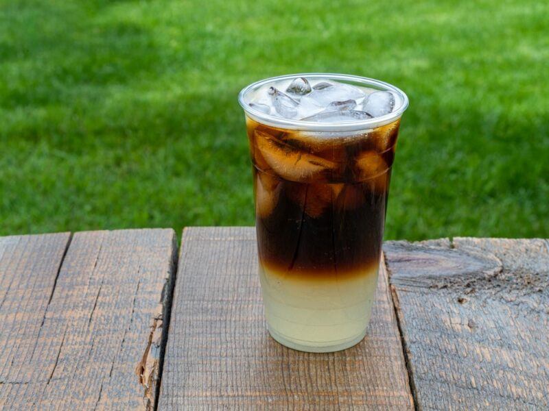 A plastic mug containing Guinness and Sprite, on a table in front of grass