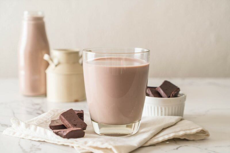 A small glass containing a Guinness milk chocolate cocktail, next to some pieces of chocolate and containers of milk in the background