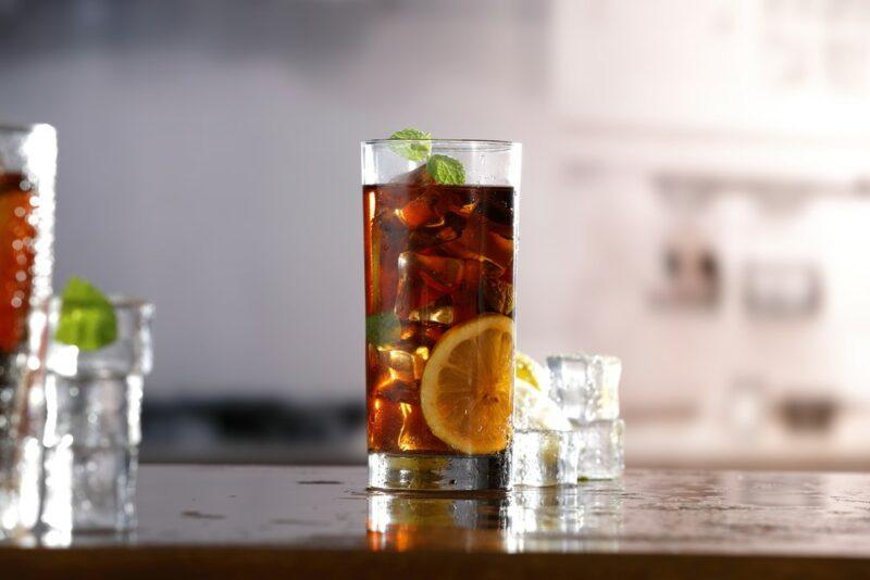 A tall glass containing Long Island iced tea on a bar, with a second such glass off to the side