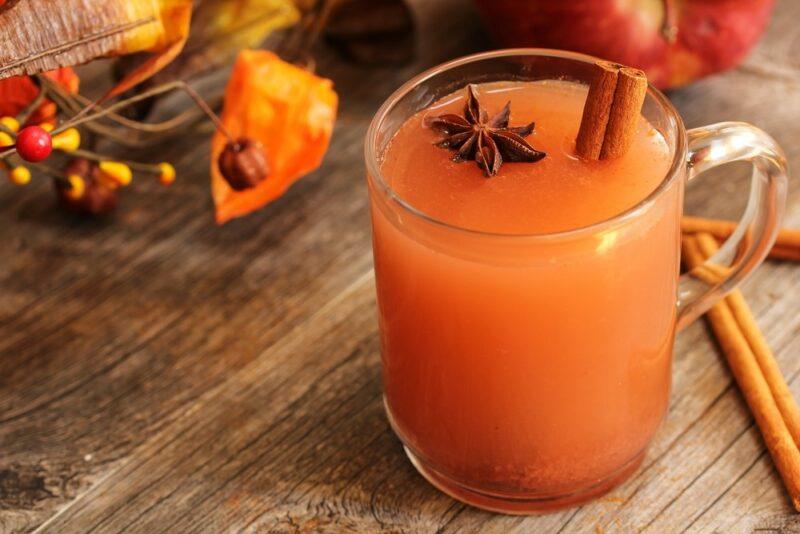 A glass mug containing a Fireball apple cider cocktail with some fall decorations on the table