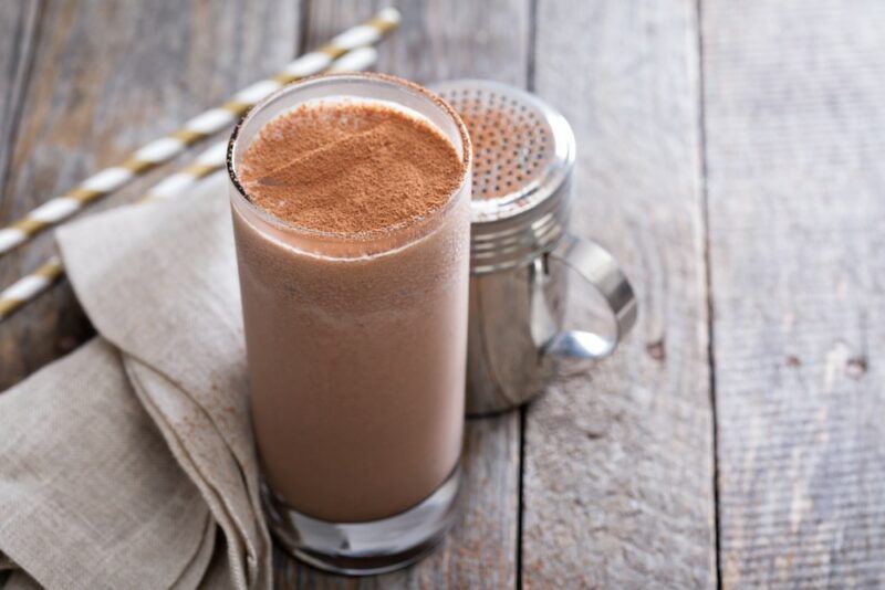 A tall glass of a Jamaican Guinness punch on a wooden table, with chocolate sprinkles as a garnish