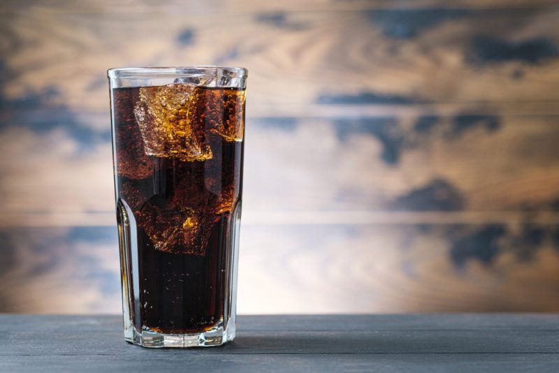 A tall glass of Roy Rogers cocktail against a mottled brown and blue background