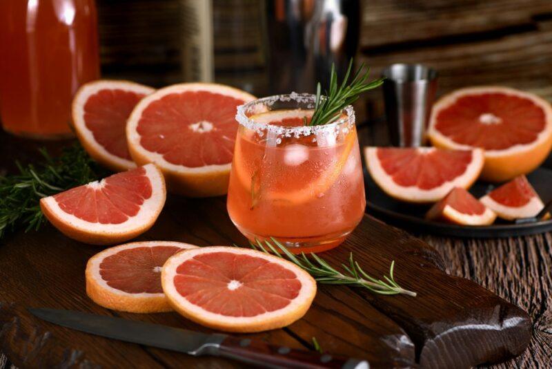 A glass of paloma cocktail on a table, with slices of grapefruit all around