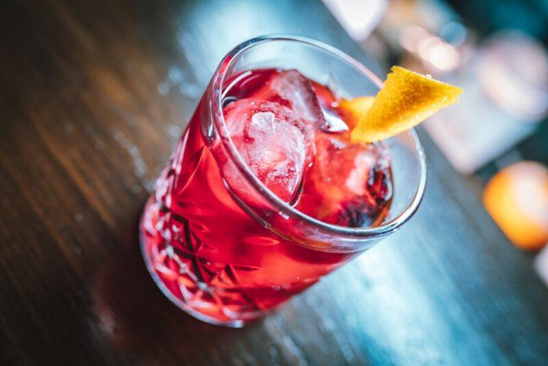 A glass of a red rosita cocktail on a bar with a lemon garnish