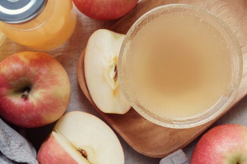 A glass of apple cider vinegar next to some whole apples and some that have been cut open