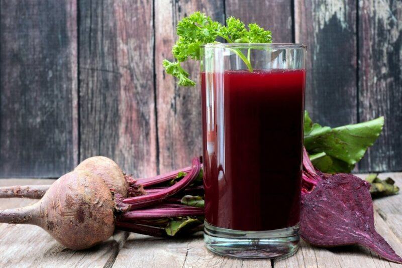 A tall glass of beet juice next to some whole beets and one that's been sliced in half