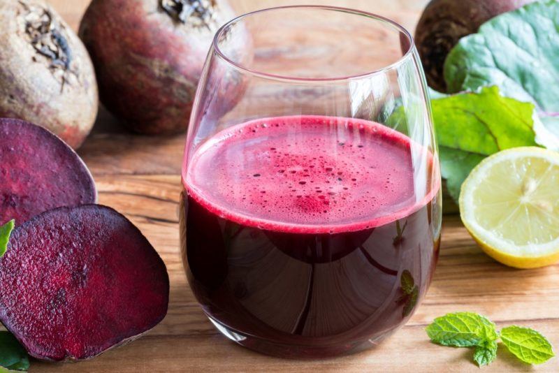 A glass of beetroot juice on the table next to some beetroots and limes