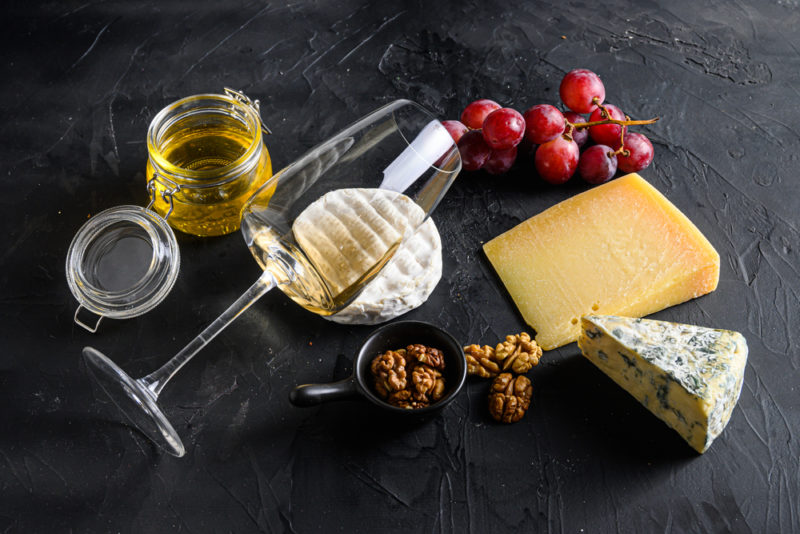 A glass of chardonnay partly tipped over, next to cheese, nuts, grapes, and honey