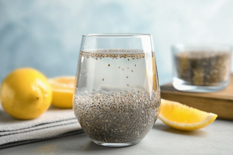 A glass of chia seeds that are soaking, with a seond one in the background, next to a whole lemon and some lemon pieces