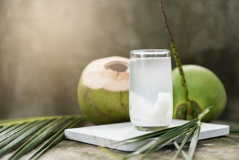 Two green coconuts behind a glass of coconut water