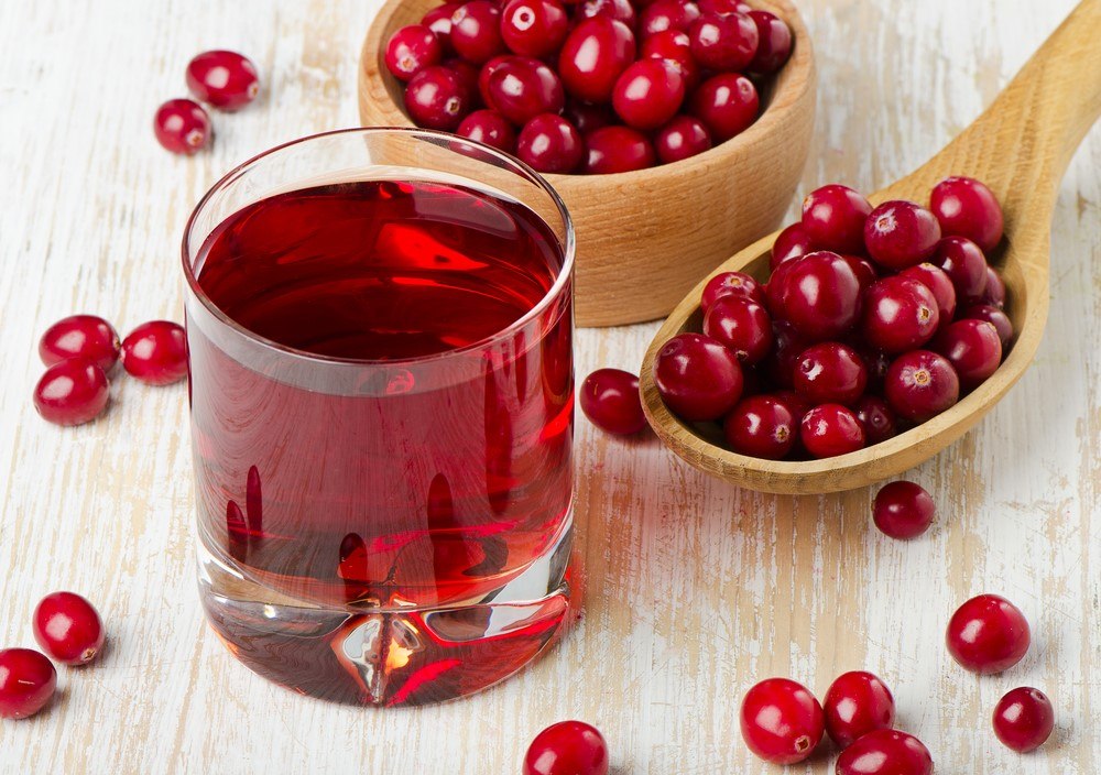 A glass of cranberry juice, with a spoon and a bowl of cranberries