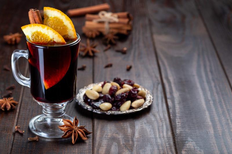 A glass of mulled wine or Glogg next to a small plate of almonds and raisins, with various spices scattered across the table