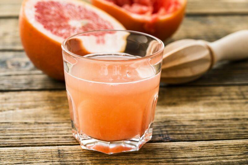 A glass of grapefruit juice on a wooden table, next to a juicer and some grapefruit halves