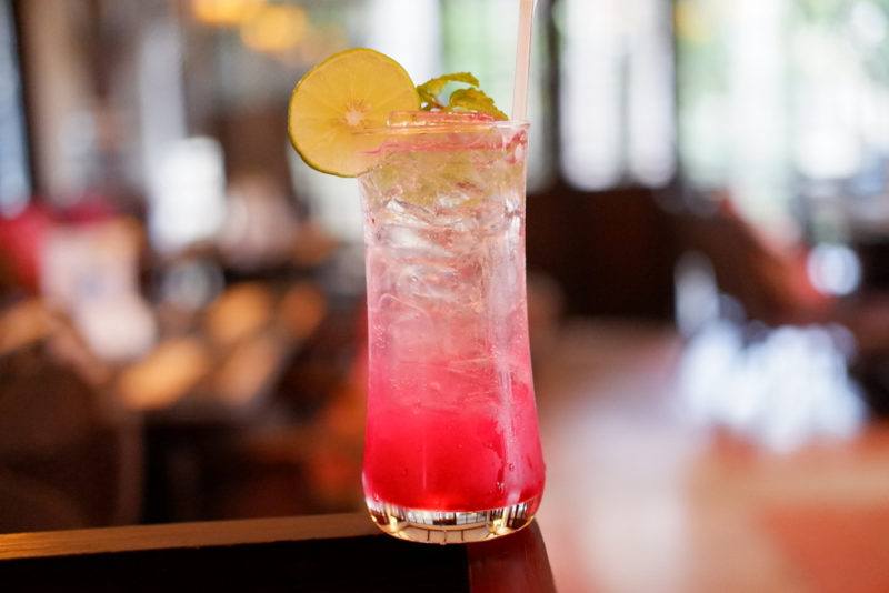 A glass of grenadine, tonic water, and lemon syrup in front of an out-of-focus bar