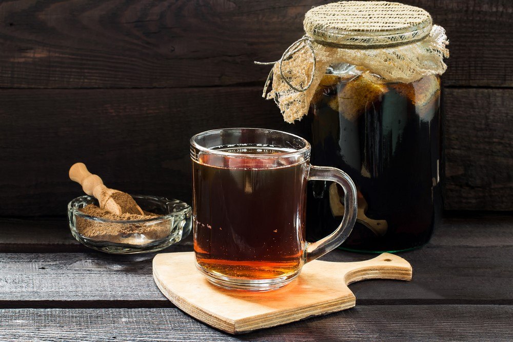 A glass of kvass on a wooden board, next to a jar of fermenting kvass