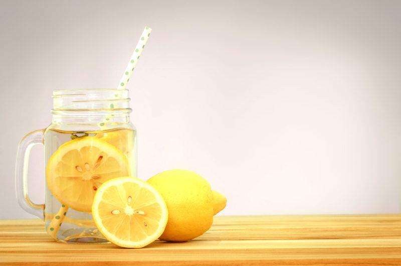 A mason jar of lemon water on a table with lemons