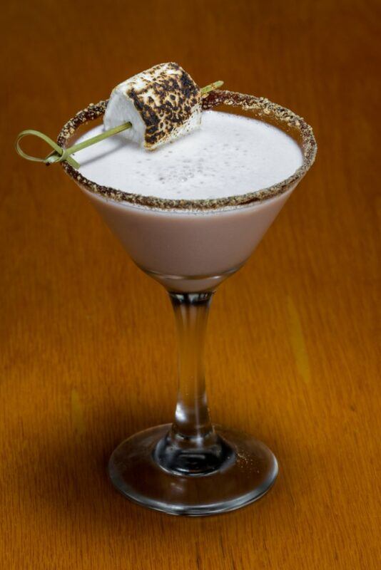 A martini glass containing a marshmallow vodka cocktail with a toasted marshmallow on top