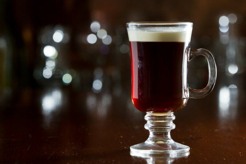 A single glass containing a mulled Guinness cocktail on a table, in front of out of focus glasses