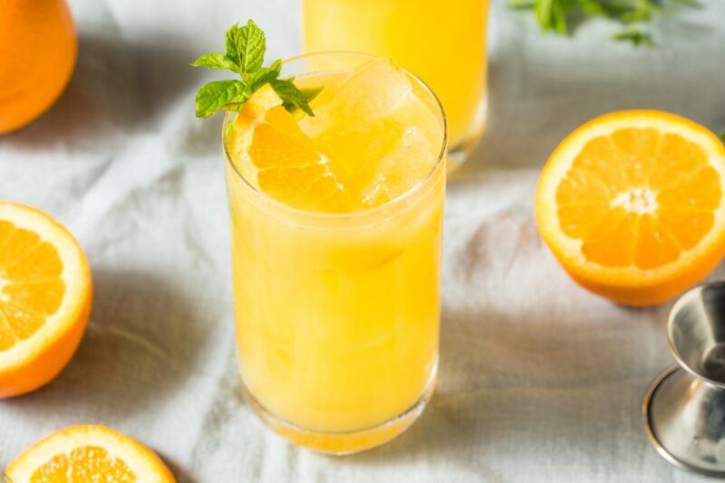 Two glasses of an orange crush cocktail next to some oranges