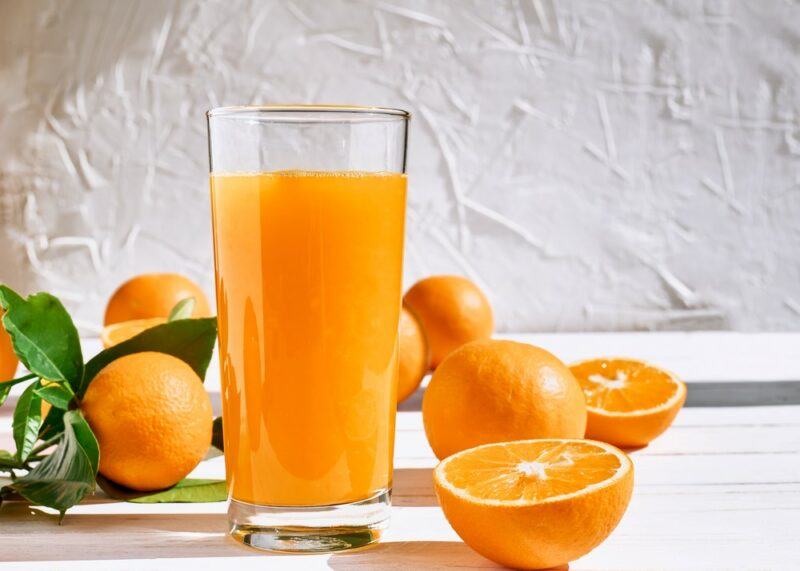 A white table with a glass of dark colored orange juice and some orange halves