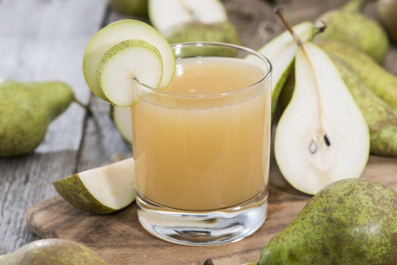 A glass of pear juice on a wooden board, surrounded by whole pears and pear halves