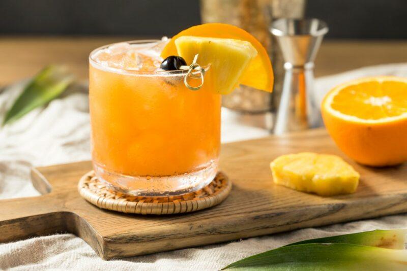 A wooden board filled with pineapple moonshine, with pineapple, oranges, and a cocktail jigger in the background