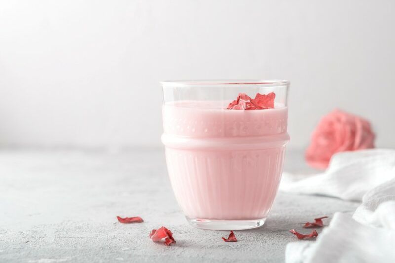 A single glass containing a pink panther cocktail, with a few petals scattered around