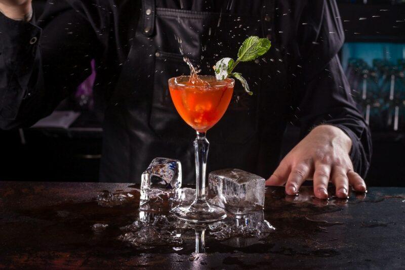 A bartender making a plum sour cocktail with ice underneath it