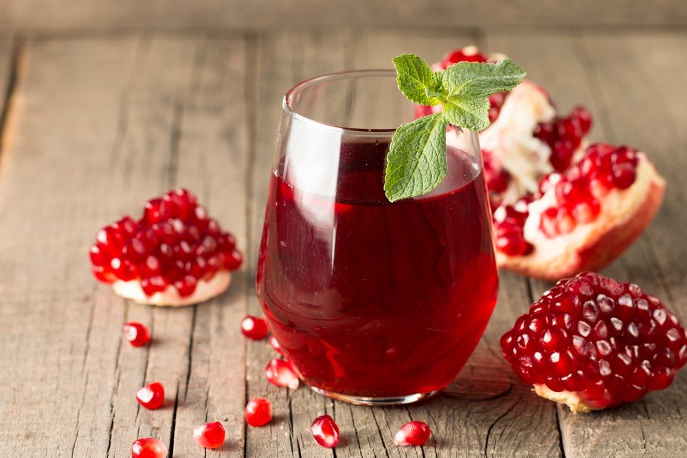 A glass of pomegranate juice next to pieces of pomegranate