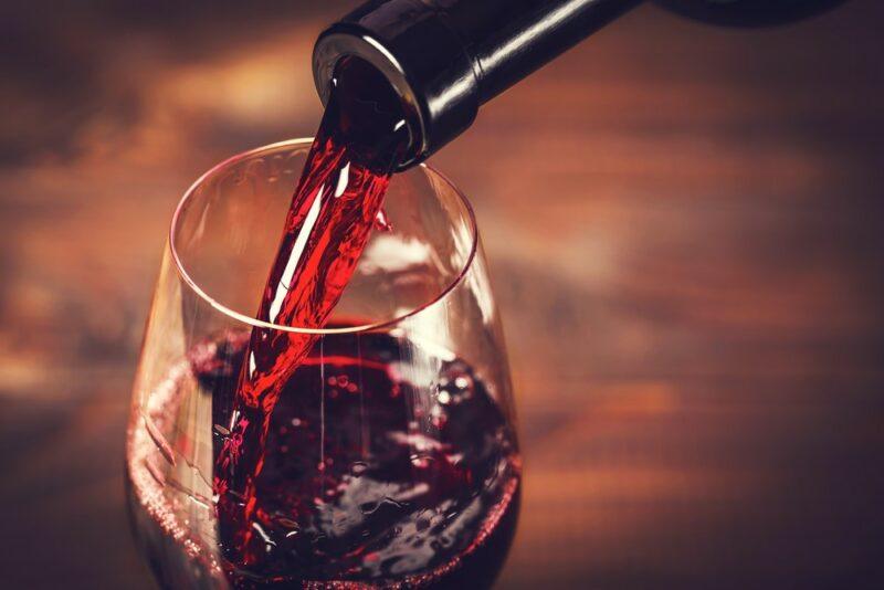 A glass of red wine being poured from a bottle on a wooden table