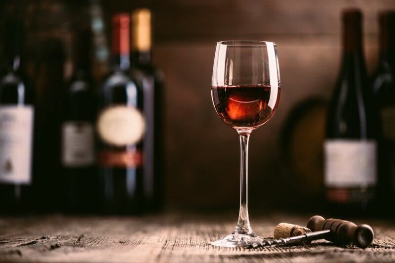 A glass of red wine on a table with many bottles of wine in the background