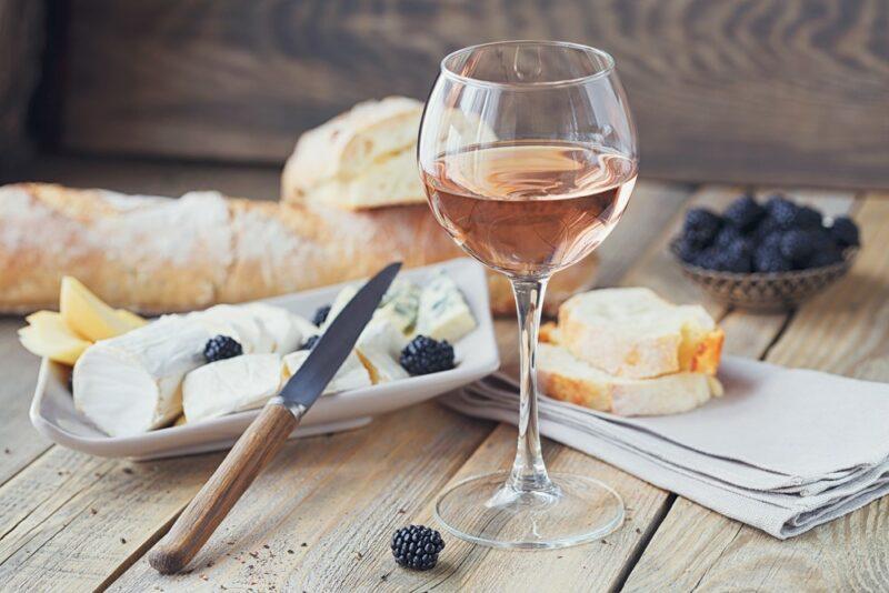 A glass of rose on a table with fresh fruit, bread, and cheese