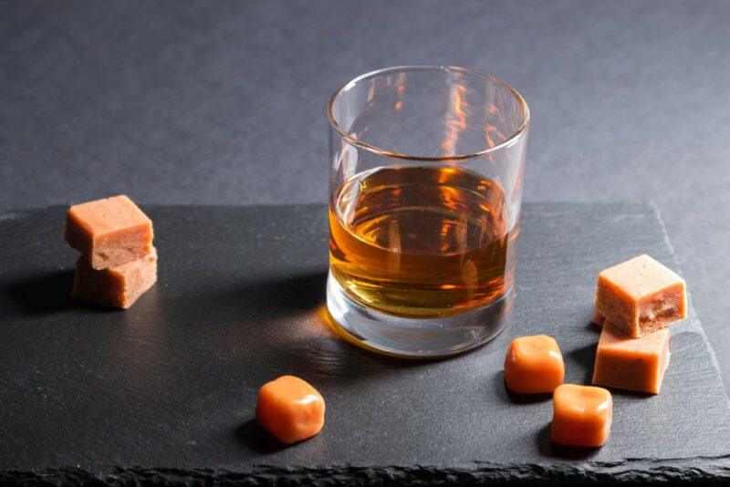 A glass containing rum and caramel liqueur, with pieces of caramel on the table