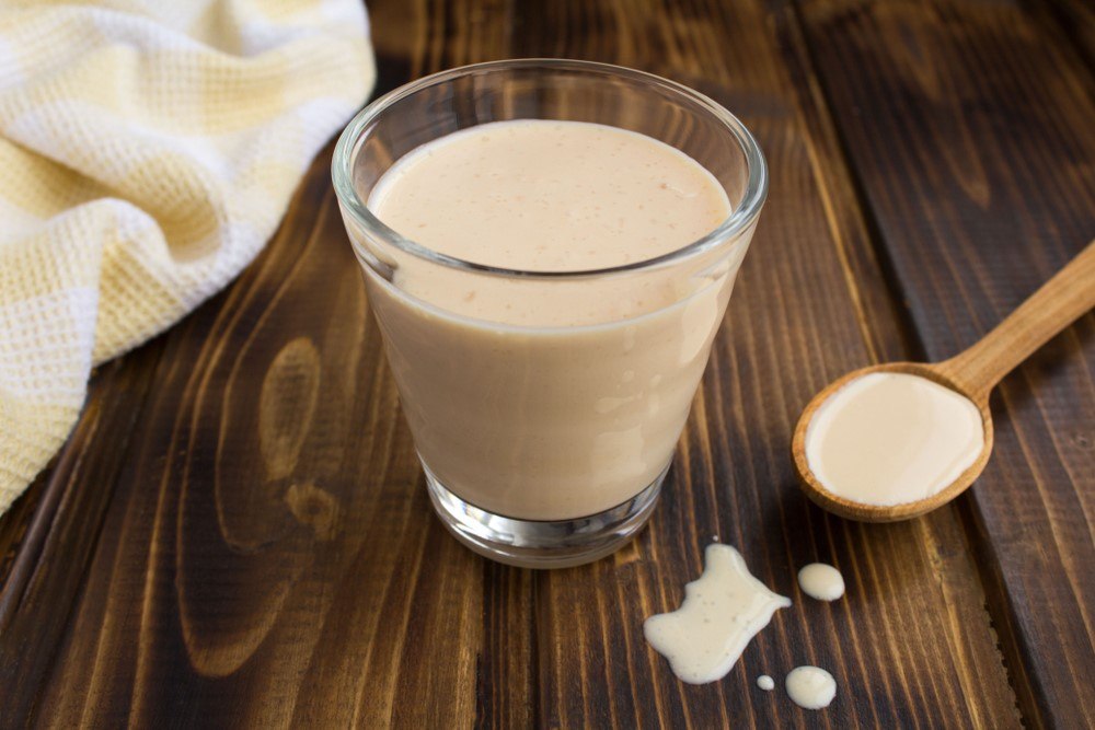 A glass of ryazhenka that is made using baked milk next to a wooden spoon