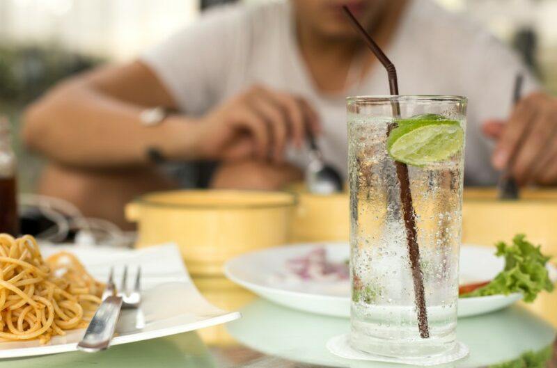 A man sitting at a table eating, with a glass of seltzer water opposite him