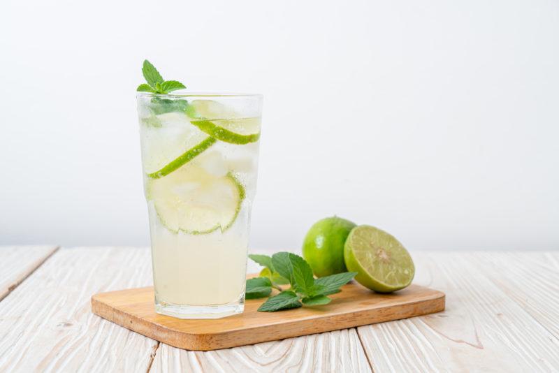 A glass of soda water with lime, with cut limes on a wooden board