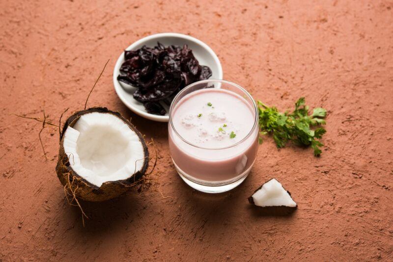 A glass of solkadhi next to a bowl of kokum fruit and half a coconut on a wooden table