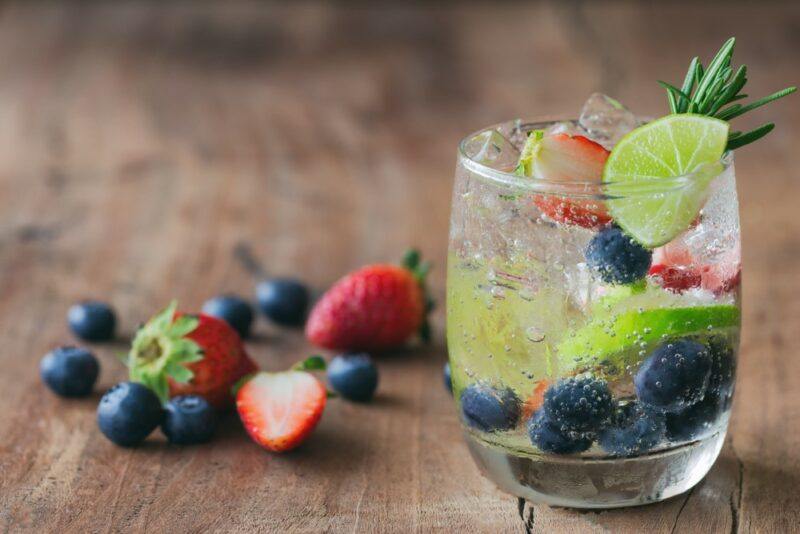 A glass of sparkling water with fresh fruit in it, plus fresh fruit next to it