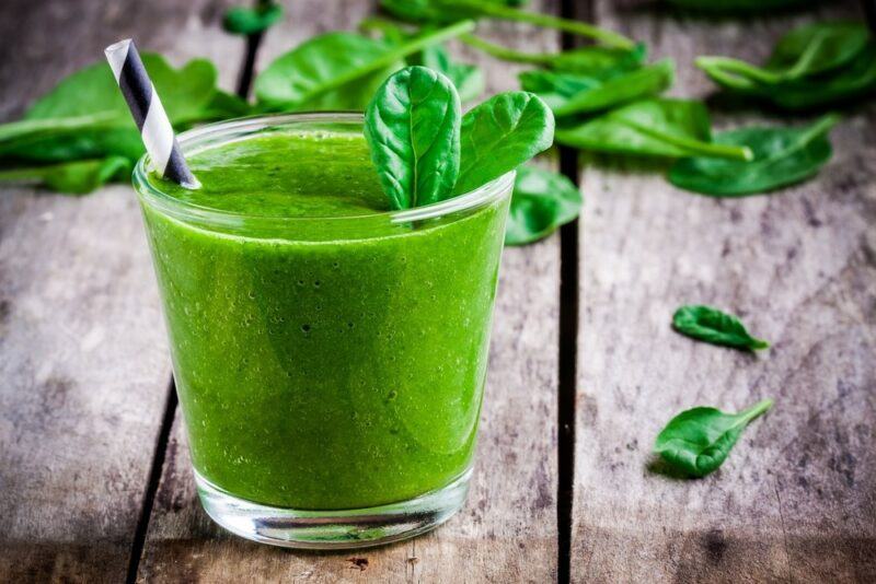 A glass of spinach juice on a wooden table with some spinach leaves scattered in the background