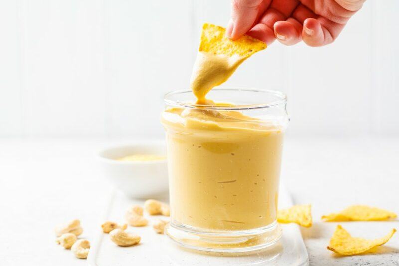 A glass filled with vegan cheese that's being used as a dip