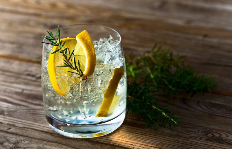 A glass of vodka tonic with ice, lemon, and rosemary