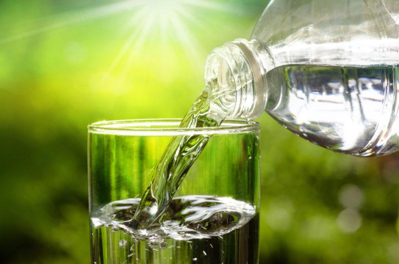 A glass of water being poured from a bottle outside in the sunlight