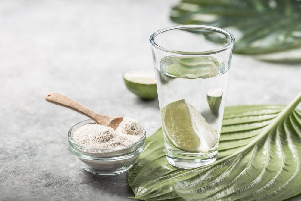 A glass of water next to a bowl of collagen powder on top of leaves