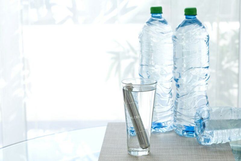 A glass of water with an alkaline filter, next to a few bottles of water on a table